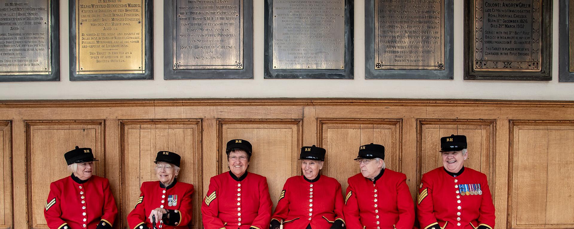 A group of female Chelsea Pensioners are sat laughing together on the colonnade at the Royal Hospital Chelsea